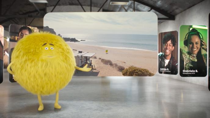 A fuzzy yellow creature stands in front of screens