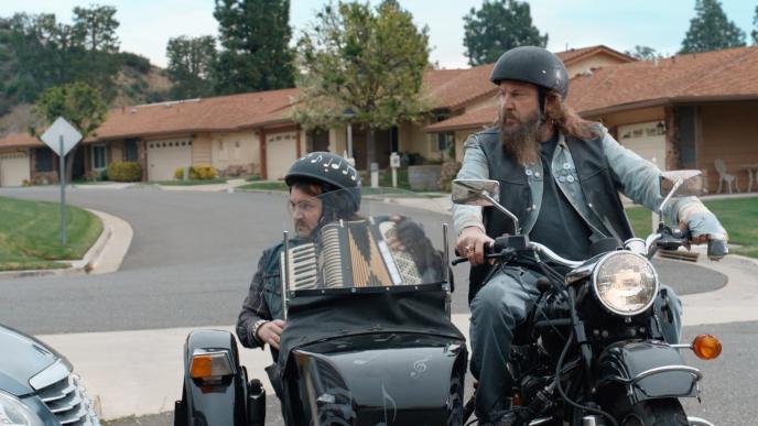 Two men on a motorcycle and sidecar - the one in the sidecar is playing an accordion