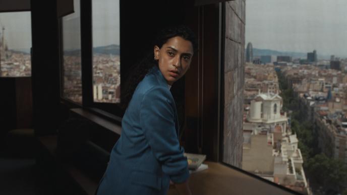 A woman stands in an office with the view of a city behind her