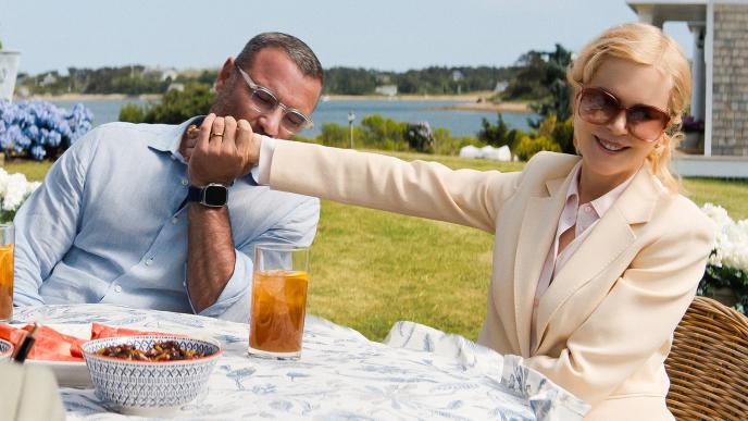 A well dressed couple at a table outside. The man kisses his wife's hand