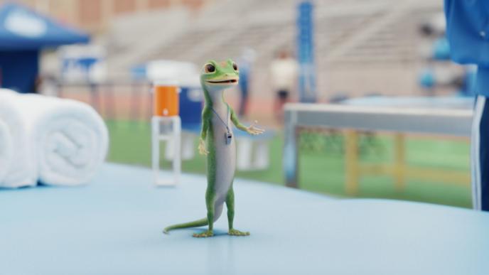 The animated GEICO Gecko stands on a training table on a football field