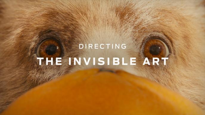 A still showing a photo-realistic CG bear's face behind an orange with white text over the top.
