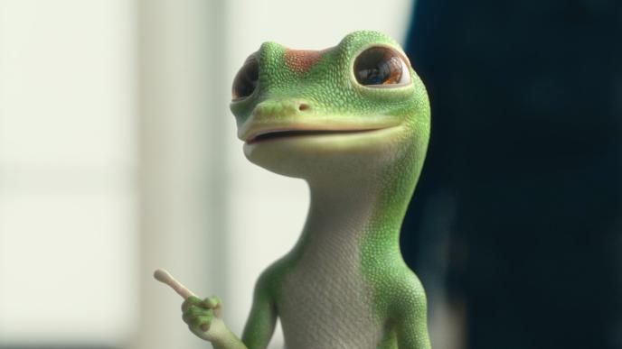 A close up of the CG animated GEICO Gecko who is standing with a grin on his face and pointing his finger