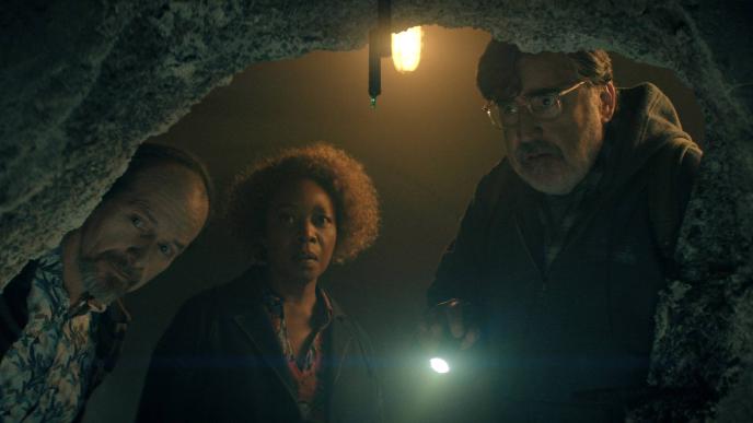 Three people look into a dark opening, holding flashlights