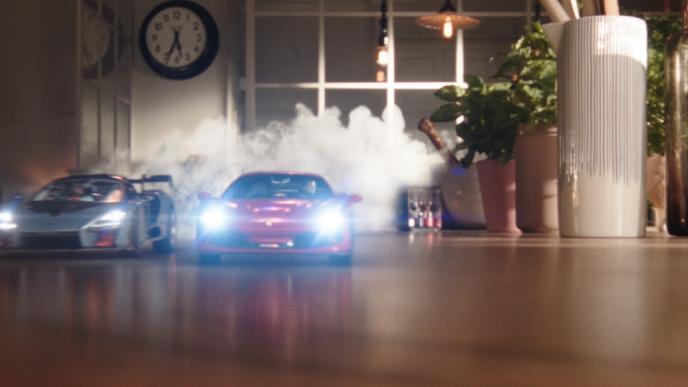 two toy cars racing in a living room. the headlights are on and there is smoke coming from the back of the cars