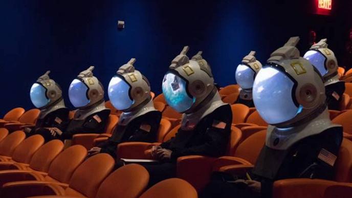 astronauts in a cinema with nebula visuals on their helmets sitting in orange seats