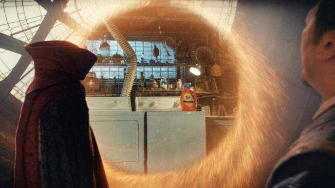 sorcerer supreme wong and doctor strange's cloak looking at a bottle of tide laundry gel sitting on a washing machine through an inter-dimensional portal