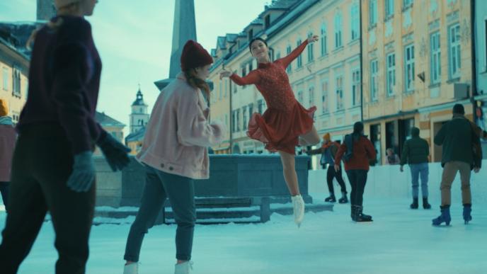 a professional ice skater in a red dress suspended in air. there are people ice skating amongst them