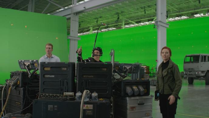 film set surrounded by green screen. actors chris evans, mark ruffalo and scarlet johanssen are standing side by side next to a machine