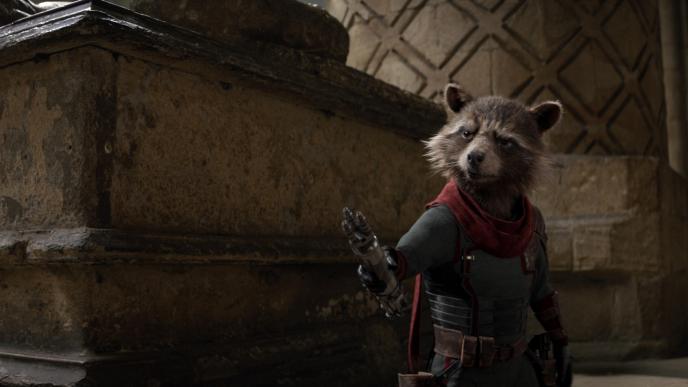 cg animated rocket the racoon wearing avengers armour suit and cape while holding up his cybernetic arm with a stern expression on his face