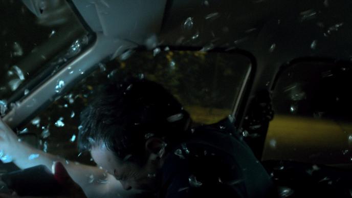 interior view of a car crash with a person closing their eyes as glass shatters around them