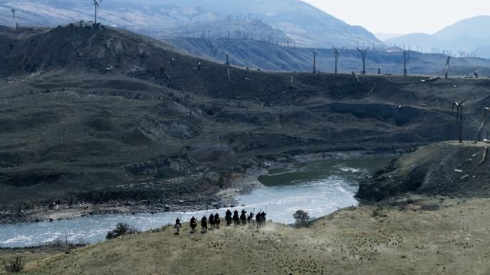 a large river winding through mountainous terrain covered in wind turbines as a group of people stand by the river