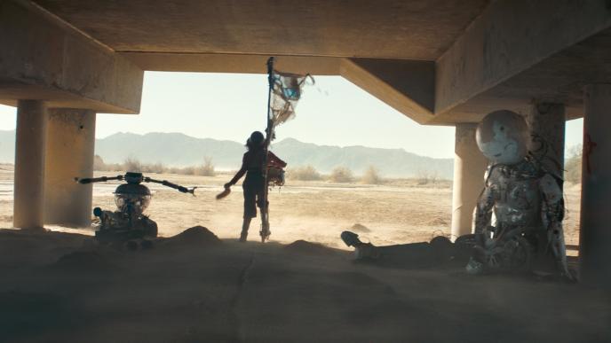 person standing in shade under a concrete bridge surrounded by broken and abandoned amusement attractions