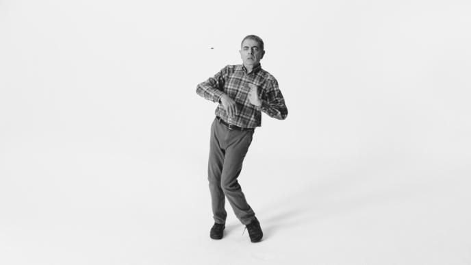 actor rowan atkinson dancing with a confused look as a bee flies nearby