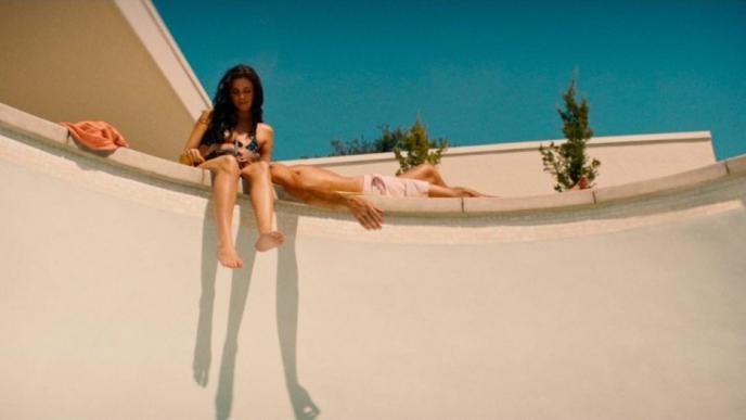 a couple lounging at the edge of an empty swimming pool