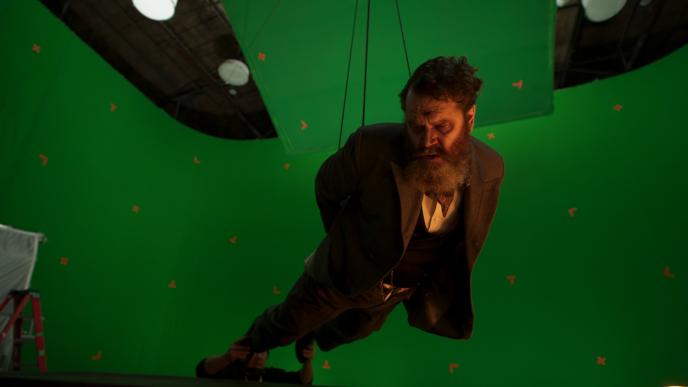 A actor suspended in a harness, shooting motion capture in forced perspective