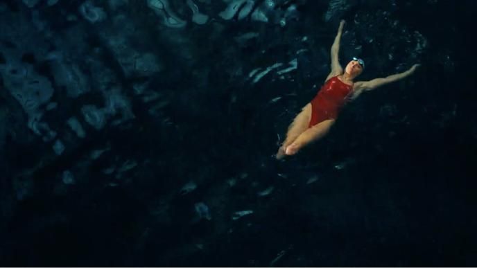 A female swimmer wearing red swimming on her back in dark water.