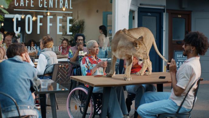 A lioness stands on top of an outside cafe table while patrons looked shocked