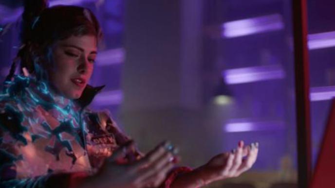 A woman sat in a room lit with purple lights, she is looking at her hands.