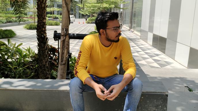 A man wearing a yellow jumper is sat on a bench in a courtyard.