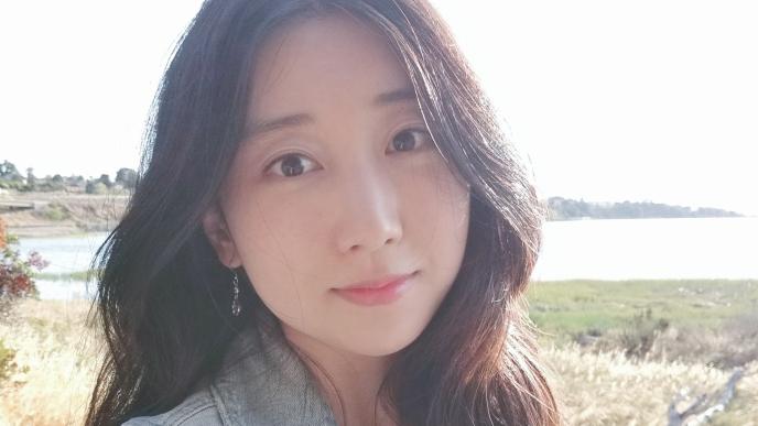 A woman taking a selfie in a field with a river in the background.