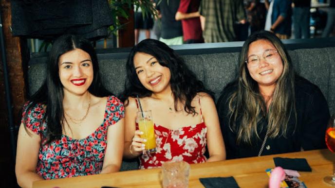 Three women sat in a booth at a bar the middle woman is holding a drink.
