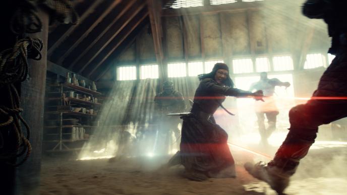 A woman fighting two men with glowing red swords, they are in a dust-filled dilapidated buidling.