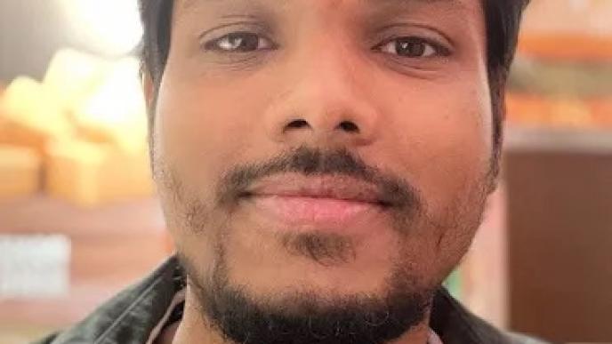 A man wearing a dark coloured shirt is smiling at the camera. 