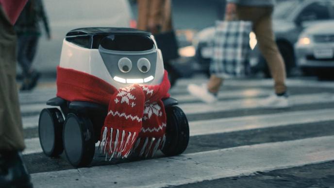 A roboto smiles at is crosses a cross walk with a holiday scarf on 