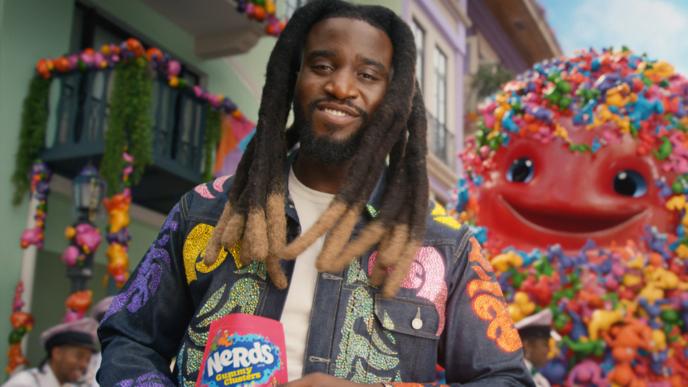 Singer Shaboozey holds a bag on Nerds Gummy Clusters while the 3D animated gummy monster appears behind him 