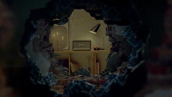 A partially destroyed wall shows a bedroom with a Marshall speaker sitting on top of a desk