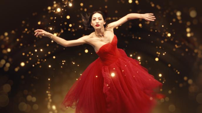Woman in flowing red dress posing dramatically amid glowing golden lights against a dark background.
