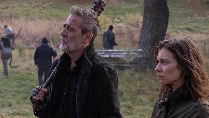 Negan and Maggie Greene from The Walking Dead: Dead City stand alert in a grassy field while others work in the background, creating a tense, post-apocalyptic atmosphere.
