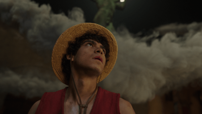 Luffy wearing a straw hat looks upward as thick smoke billows behind them in a dimly lit setting.