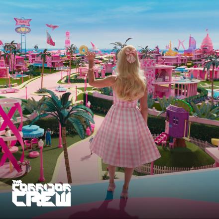 A woman stands looking out over a landscape filled with pink houses, she is waving.