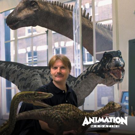 A man sat at a desk surrounded by CGI dinosaurs, some on the desk and one large on poking its head through a window.