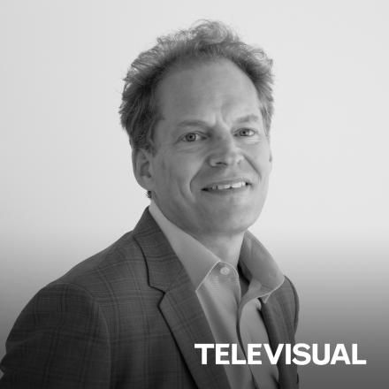 A black a white photo of David Kassler with a white Televisual logo in the lower right hand corner