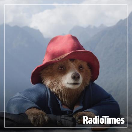 Paddington climbs over the top of a ledge in his red hat and blue coat, a white Radio Times logo is overlaid in the bottom right corner